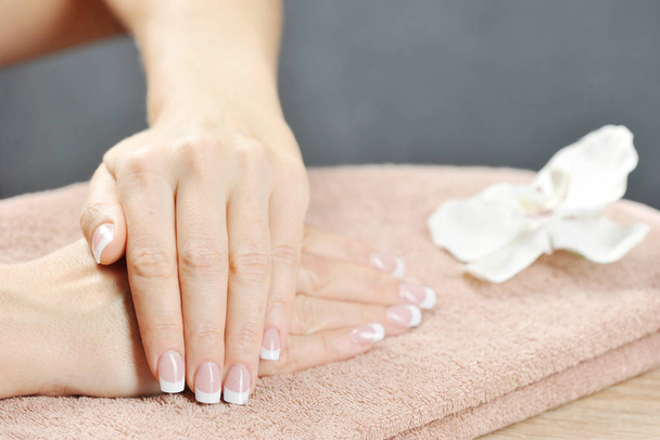 French manicure. In the frame, two women's hands rest on a towel. Near the white orchid flower. Close-up.  - Foto, Imagem
