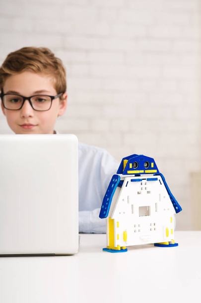 Шкільний хлопчик, що друкує план інноваційної моделі робота на ноутбуці
 - Фото, зображення