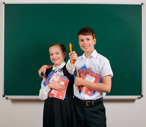 Емоційний портрет школяра і школярки, що позує з тренажерами, ручками, олівцями та іншими шкільними приладдям на фоні дошки назад до школи та концепції освіти
 - Фото, зображення