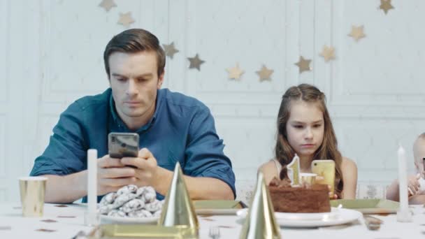 お祝いのテーブルの上に携帯電話を保持している深刻な父と娘. - 映像、動画