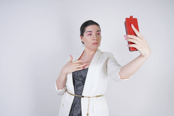 encantadora mezcla de raza más mujer de tamaño en una chaqueta de negocios blanca de pie con teléfono inteligente en la mano sobre fondo blanco en Studio
 - Foto, imagen