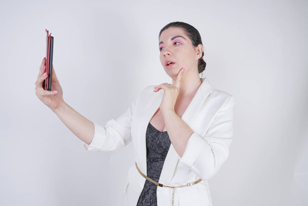 encantadora mezcla de raza más mujer de tamaño en una chaqueta de negocios blanca de pie con teléfono inteligente en la mano sobre fondo blanco en Studio
 - Foto, Imagen