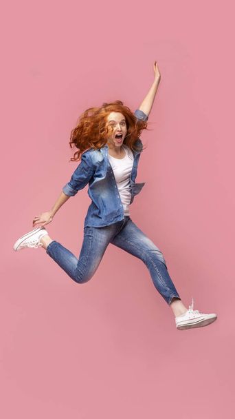 Pozitív vörös hajú lány átugrik rózsaszín stúdió háttér - Fotó, kép