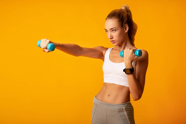 Young Woman Doing Dumbbell Boxing Workout On Yellow Background - Foto, afbeelding