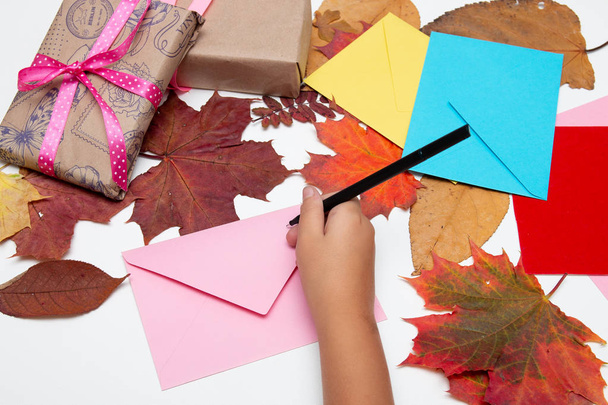 children's hand writes on an envelope on a white table, postcards, envelopes, Thanksgiving, birthday, holiday, congratulations, autumn leaves on the background, copy space - Foto, afbeelding
