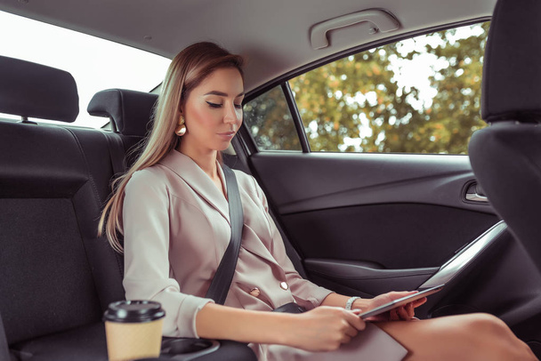 business lady girl suit, passenger in interior taxi business class VIP. In hand tablet, online application on Internet, reads watches video on screen, working on road, movement in car summer city. - Valokuva, kuva