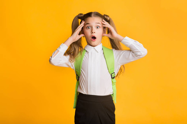 Shocked Elementary Student Girl Clutching Head Over Yellow Background - Foto, immagini
