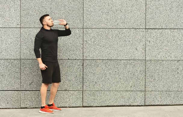 Atleta assetato di acqua potabile mentre in piedi contro muro di cemento grigio
 - Foto, immagini