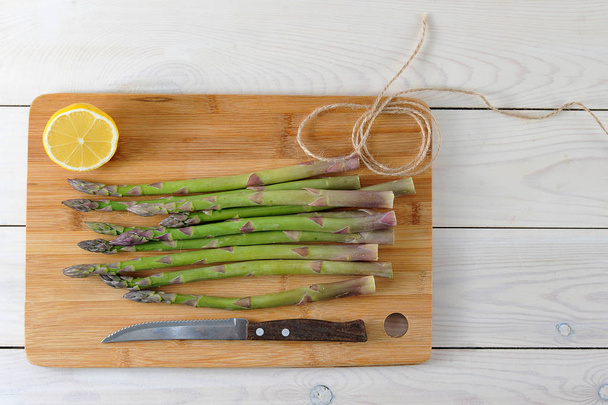 Fresh asparagus on a wooden tray. Next knife and half a lemon. Light background. View from above. Close-up. - Foto, immagini