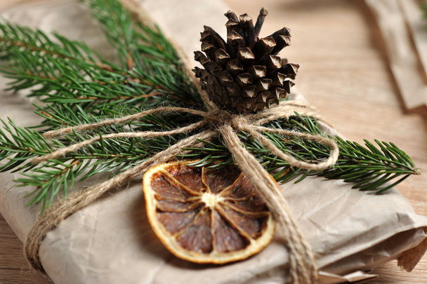 Christmas gift wrapped in craft paper. The gift is decorated with a spruce branch, a cone and a slice of dry orange. Close-up. Macro shooting. - Φωτογραφία, εικόνα