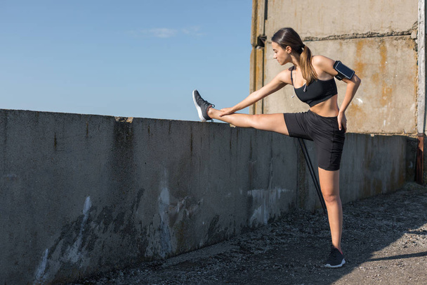 Тонкая атлетическая девушка выполняет упражнения на растяжку на крыше незавершенного здания, городского фона. Наслаждается тишиной и свободой
. - Фото, изображение
