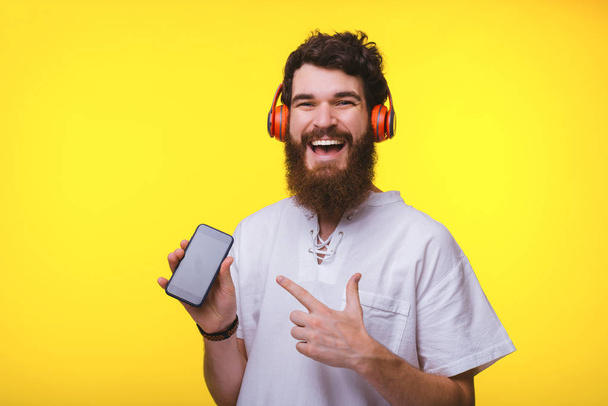 Zdjęcie wesoły człowiek wskazując na jego smartphone i noszenia HEA - Zdjęcie, obraz