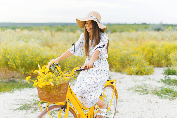 Photo of pretty young woman, in dress and hat, on bicycle in a f - Foto, Bild