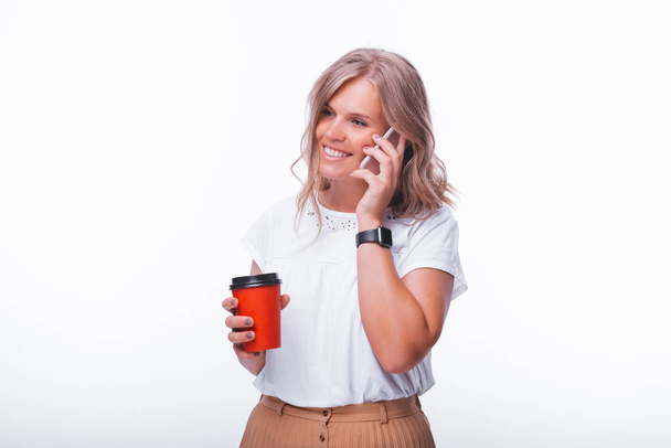 eine junge blonde Frau, die telefoniert, während sie eine Tasse mit  - Foto, Bild