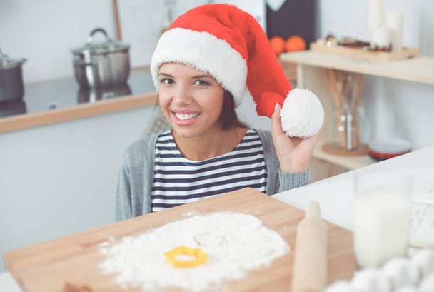 Woman in santa hat making christmas cookies in the kitchen - Zdjęcie, obraz