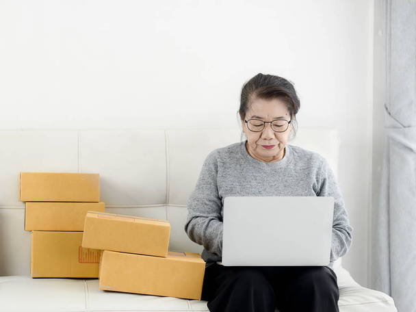 Asian senior woman using laptop while selling online with packag - Foto, afbeelding