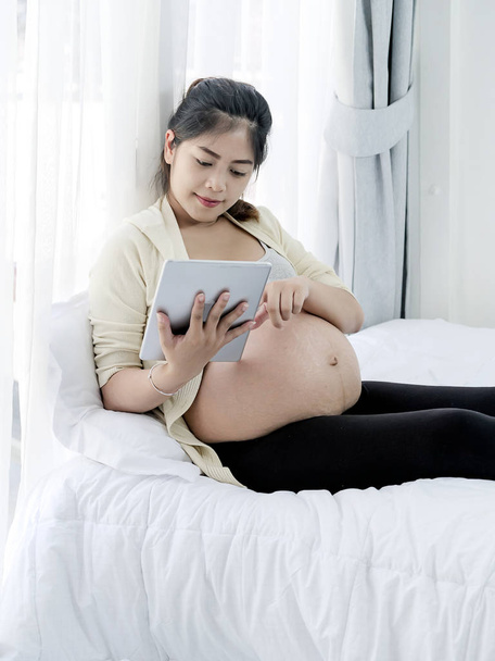 Asian pregnant woman using tablet on bed at home, lifestyle conc - Foto, Imagen