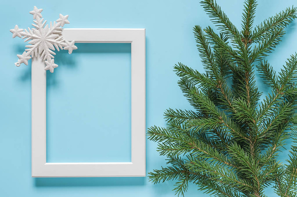 White frame with decoration snowflake and green spruce branch on blue background. Concept Merry christmas or Happy new year. Top view Flat lay Mockup Template for your design, card, invitation. - Photo, image