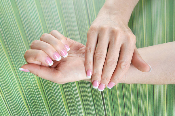 Female hands with french manicure on green background. Close-up.  - Zdjęcie, obraz