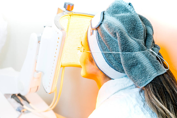 Beauty-Spa-Patientin unterzieht sich einer geführten Fotomodulation für eine lichtbasierte Gesichtsbehandlung, als Anti-Aging-Behandlung und zur Heilung von Sonnenbrand. - Foto, Bild
