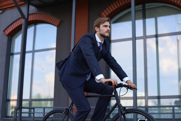 Handsome businessman riding bicycle to work on urban street in morning. - Foto, imagen
