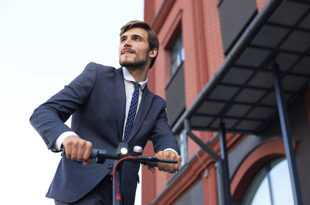 Young business man in suit riding on electric scooter on a business meeting. Ecologic transport concept. - Фото, изображение
