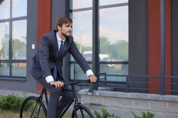 Joven hombre de negocios guapo montando en su bicicleta en la ciudad. Concepto de transporte ecológico
.  - Foto, Imagen