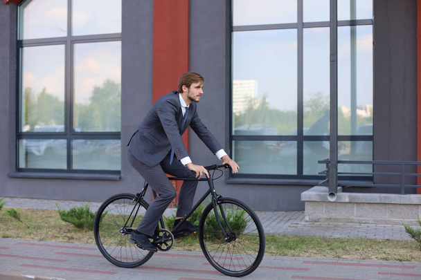Handsome young businessman riding on his bicycle in the city. Ecologic transport concept.  - Zdjęcie, obraz