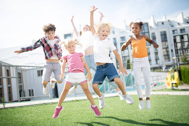 Children jumping high while having fun outside after lessons over - Foto, Imagem