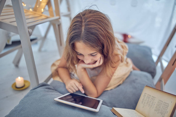 Pequeña niña de 10 años usando tableta debajo de su tienda de campaña casera en
 - Foto, imagen