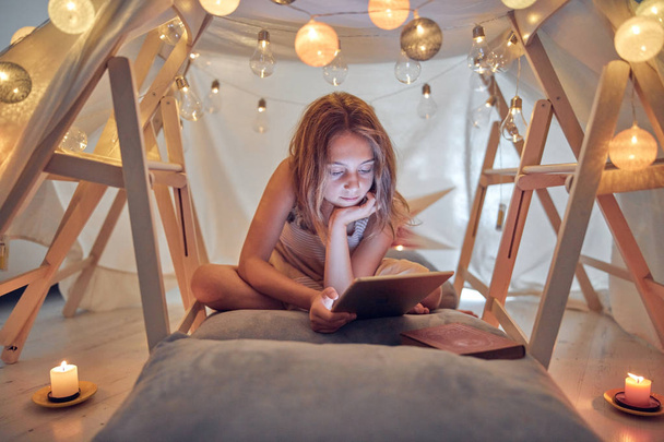 Piccola bambina di 10 anni utilizzando tablet sotto la sua tenda fatta in casa in
 - Foto, immagini