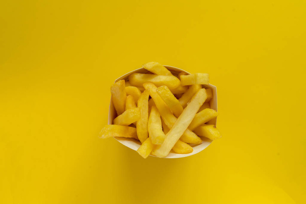 fresh fried junk potato fries come out from the paper box on color background - Fotó, kép