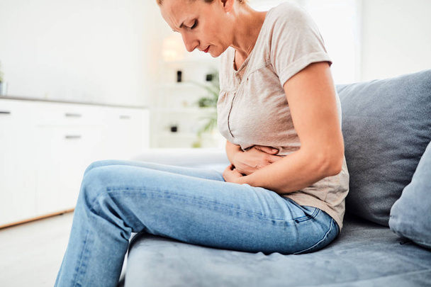 Woman with  stomach issues / problems while sitting on the couch - Photo, image
