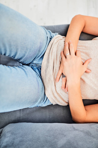 ソファに横になっている間の胃の問題/問題を持つ女性. - 写真・画像