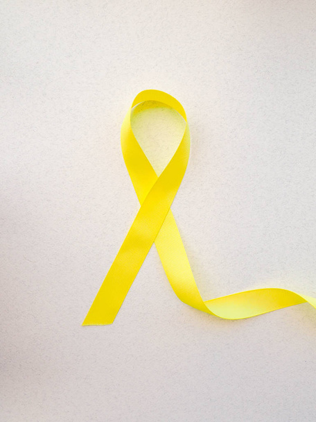 Κίτρινη κορδέλα επίγνωσης σε ανοιχτόχρωμο φόντο, κίτρινη κορδέλα συμβολικό χρώμα για το σάρκωμα του καρκίνου των οστών, μήνας ευαισθητοποίησης δισχιδή ράχη και πρόληψη αυτοκτονίας στο χέρι βοηθείας - Φωτογραφία, εικόνα