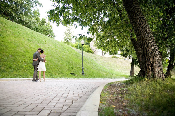 bride and groom are moving away along the alley in the park, hugging each other - 写真・画像