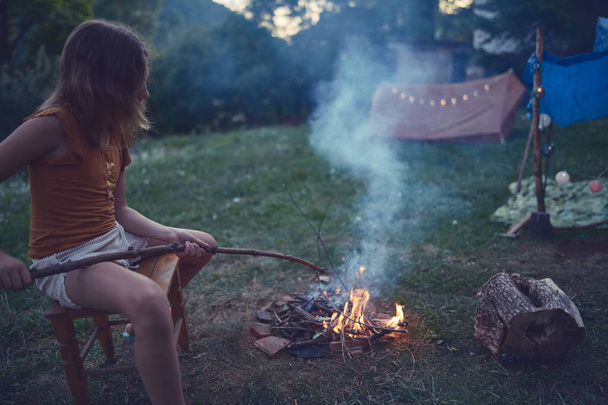 芝生の上でキャンプファイヤーをする小さな子供の女の子. - 写真・画像