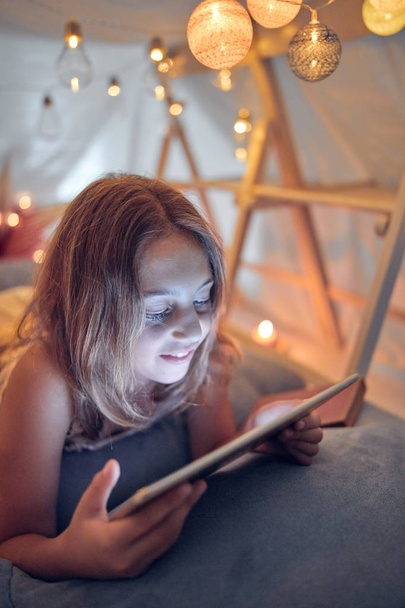 Little 10 year old girl using tablet under her home-made tent in - 写真・画像