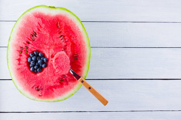 Watermelon and blueberries on white background. The process of eating watermelon with a spoon. Blueberries in watermelon. Creative food concept - Foto, afbeelding