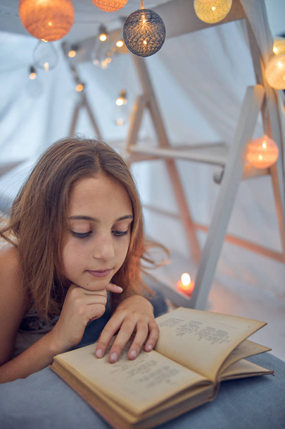 kleines 10-jähriges Mädchen liest klassisches Buch unter ihrem selbst gebastelten - Foto, Bild
