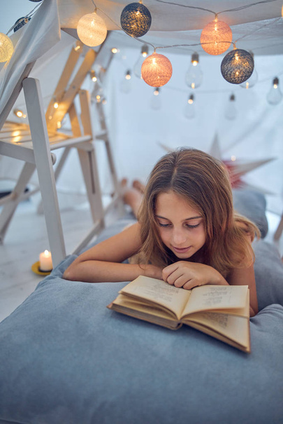 Маленькая 10-летняя девочка читает классическую книгу под домашней работой
 - Фото, изображение