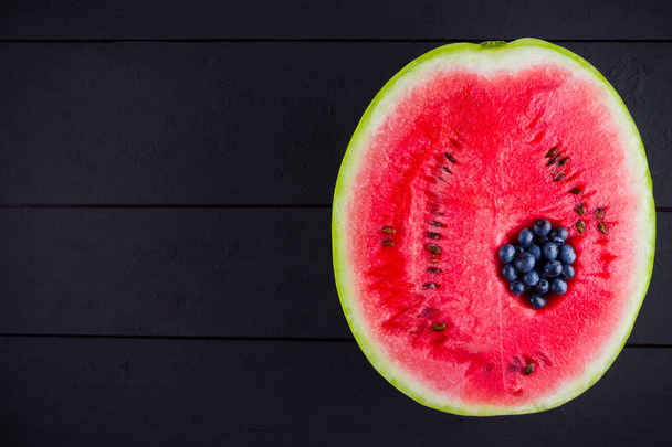 Watermelon and blueberries on dark background. Blueberries in watermelon. Creative food concept. Top view - Photo, image