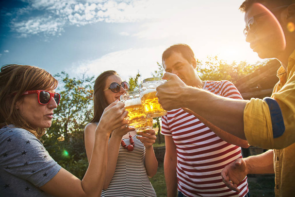 Group of young people enjoying and cheering beer outdoors. - Фото, изображение