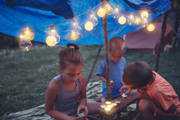 Lapset tekevät pienen teltan kynttilöillä ja lampioneilla takapihalla.
 - Valokuva, kuva