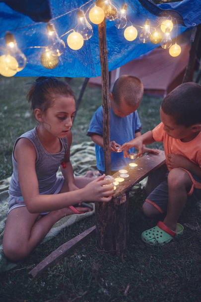 A gyerekek kis sátrat építenek gyertyákkal és lámpákkal a hátizsákban. - Fotó, kép