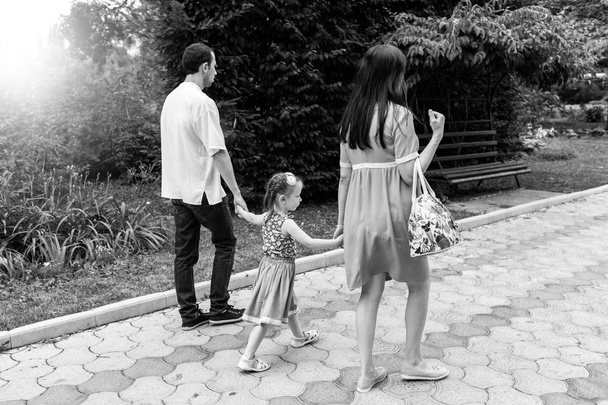 Vista trasera de la familia feliz caminando por el camino tomados de la mano y pasar tiempo en el hermoso parque verde
. - Foto, imagen