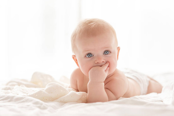 Felice bambina neonata su un letto in camera da letto bianca vicino alla finestra luminosa
 - Foto, immagini