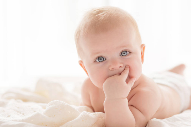 Happy little baby girl infant on a bed in white bedroom near the bright window - Фото, зображення