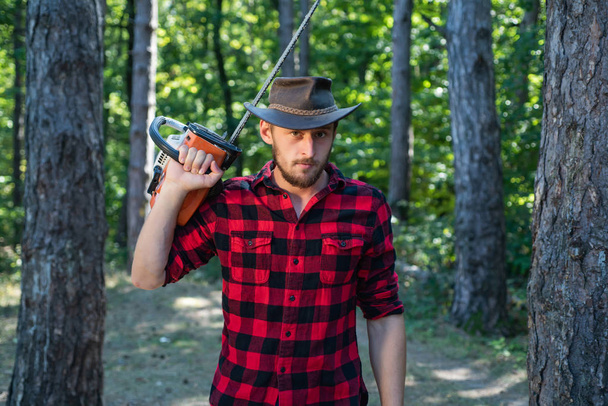 Woodcutter with axe or chainsaw in the summer forest. Lumberjack concept. - Foto, Bild