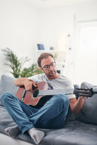 リビングルームでアコースティックギターを演奏する男. - 写真・画像